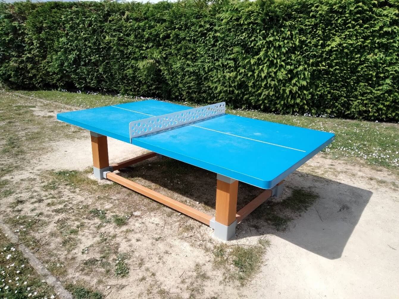 Table de tennis de table de couleur bleue, avec des pieds en bois, une haie est situé proche de la table
